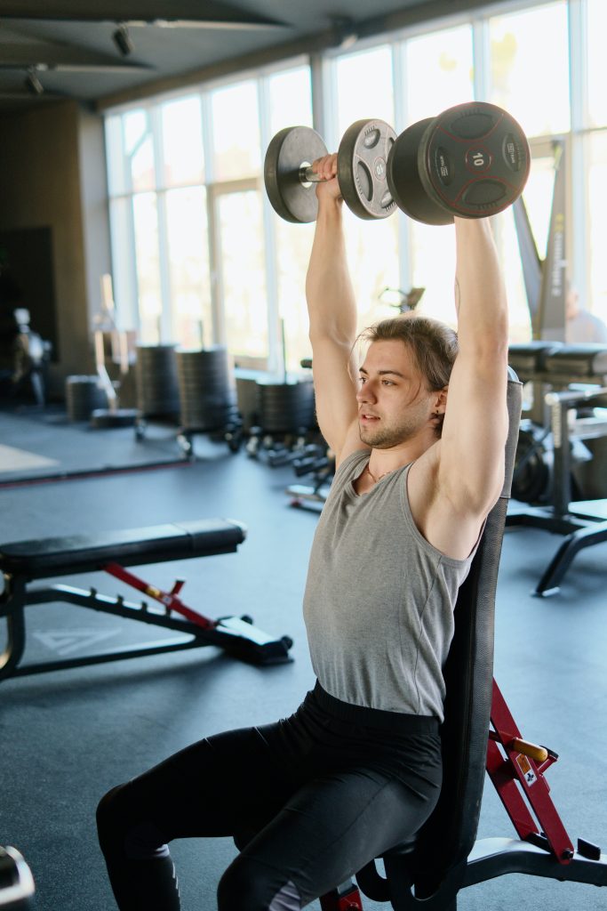 Bodybuilding. Čovek radi u teretani vežbe za ramene mišiće. 